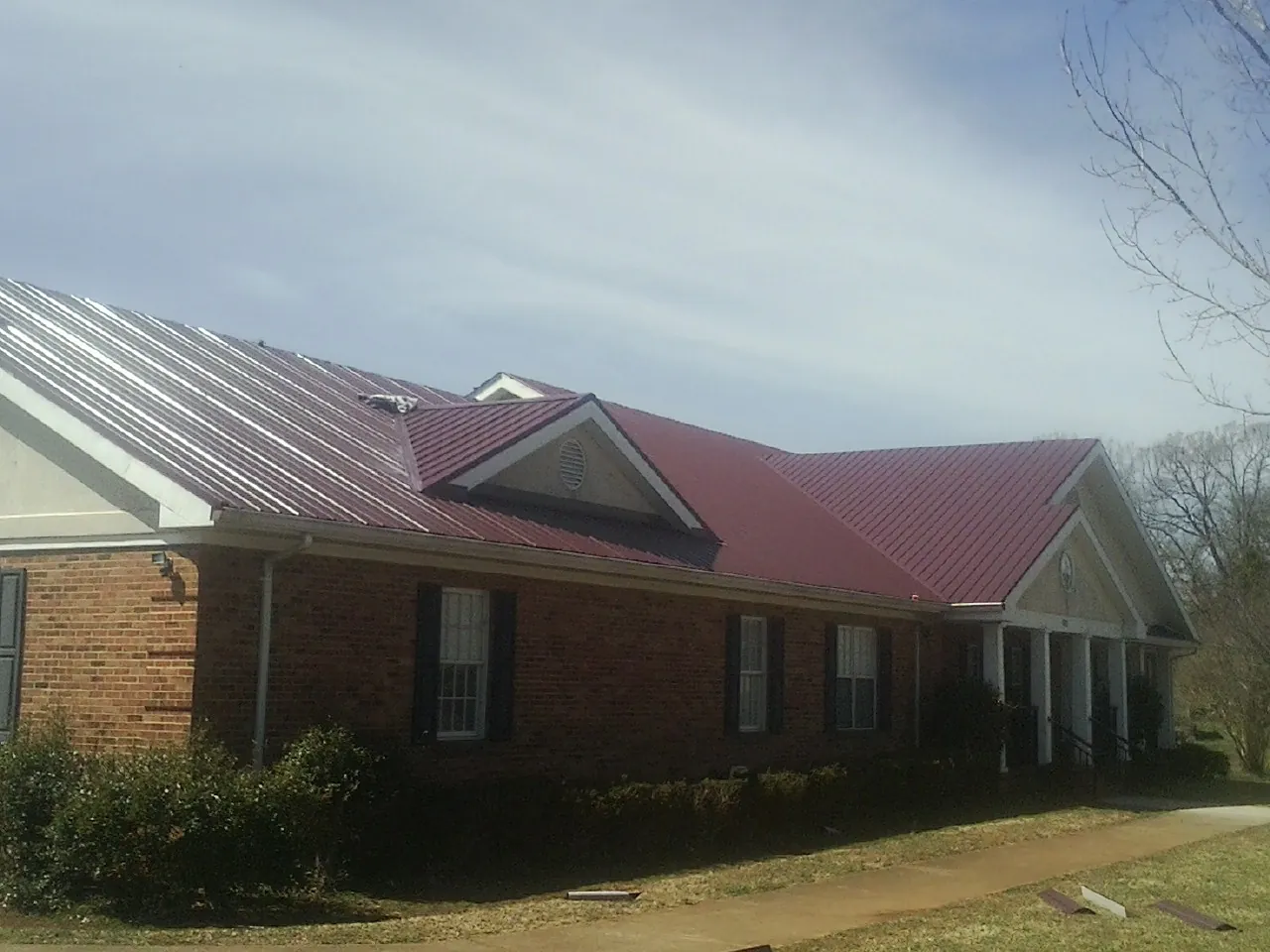 Red metal roof with gabled entries on a long brick building, from a Hail Damage Roof Repair job in Cross