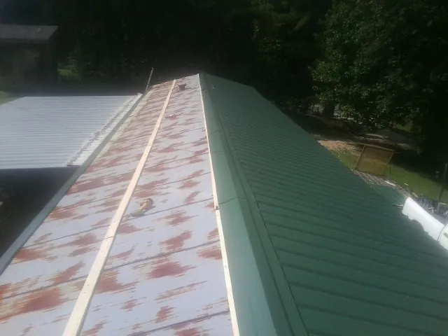 Old rusted panels beside newly installed green metal roofing — Wind Damage Roof Repair by Roofing Brothers in Cross