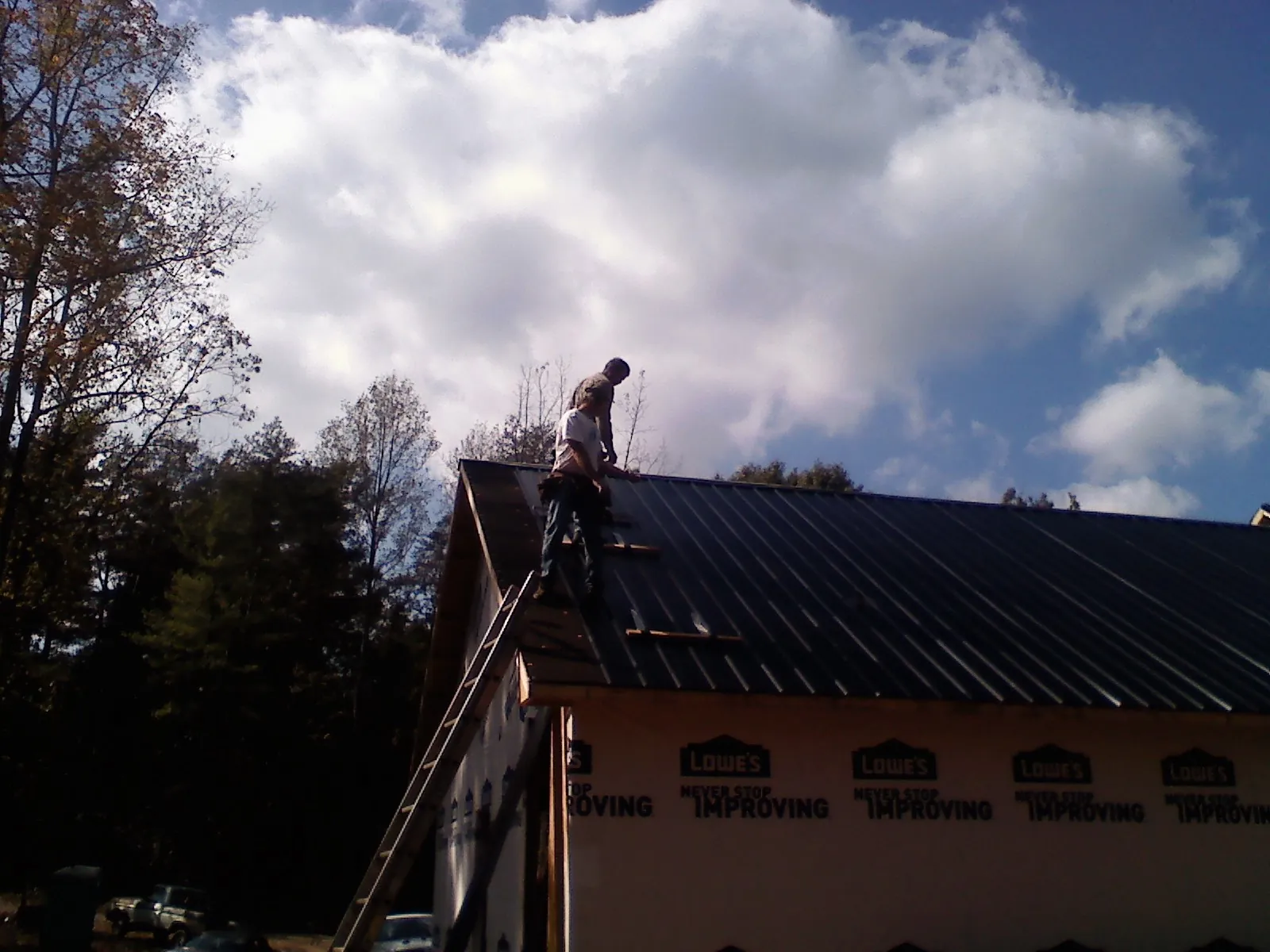 Roofer fastening dark metal panels high against a cloudy sky, from a Roof Inspection job in Cross