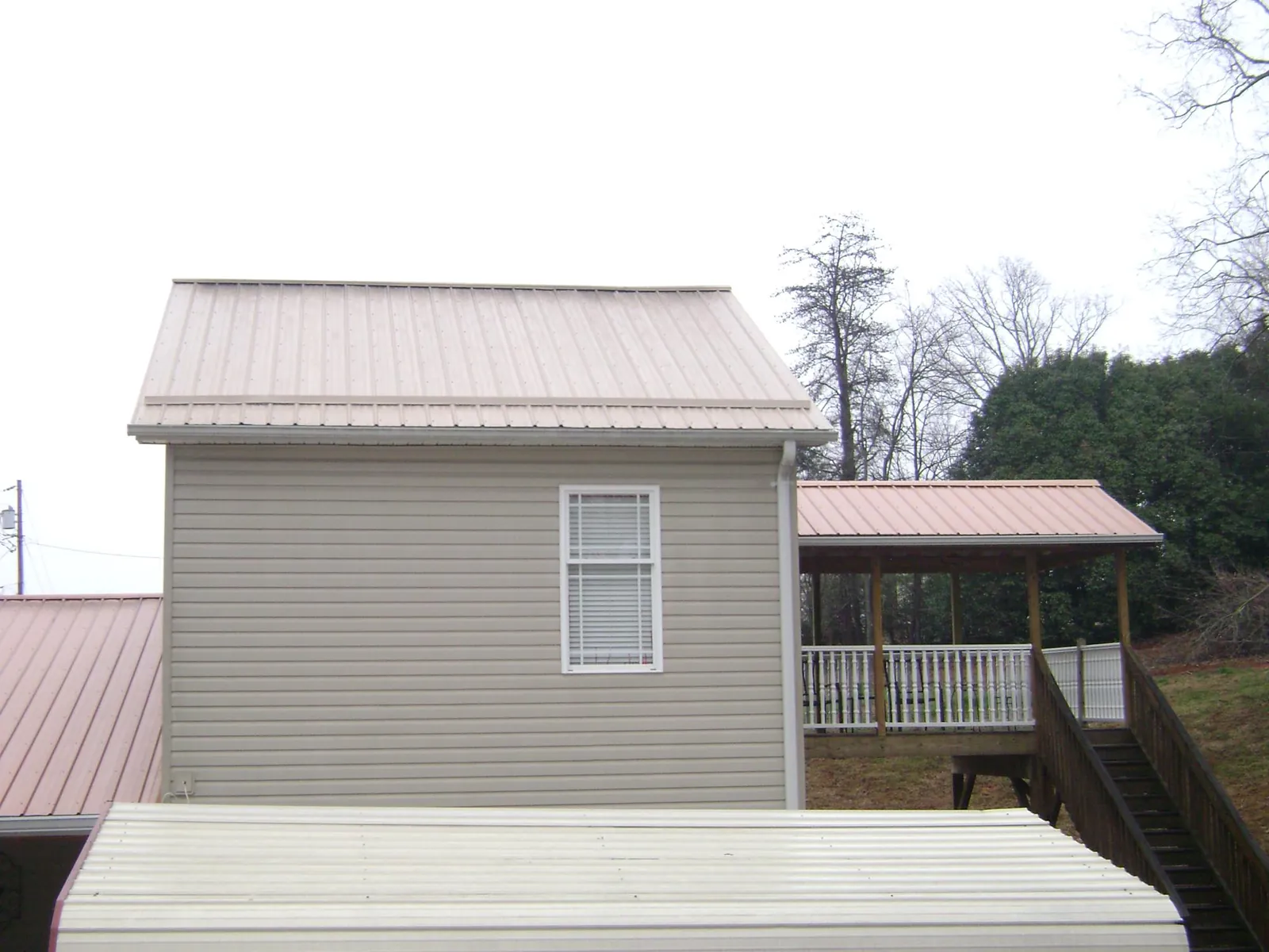 Tan metal roofs on a two story addition and attached porch, from a Roof Replacement job in Cross